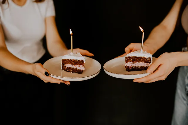 Zwei Händepaare halten Teller mit Kuchenstücken und Kerzen.