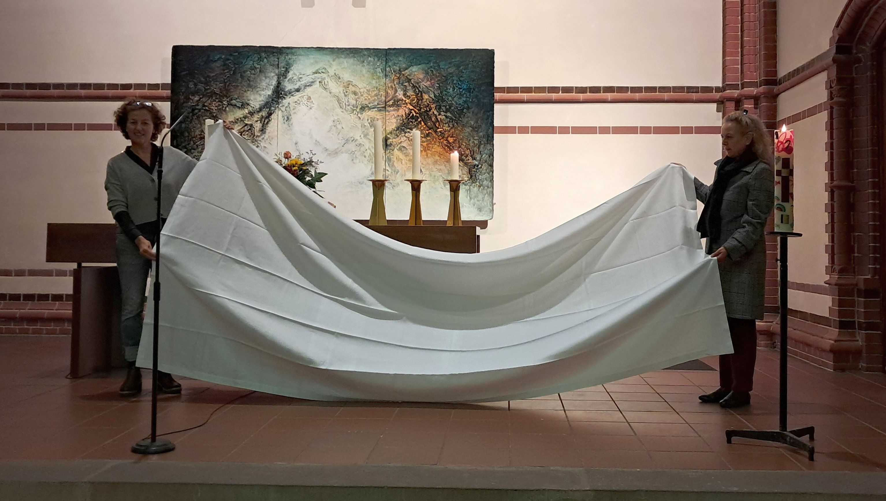 Zwei Frauen halten ein großes weißes Tuch in einer Kirche.