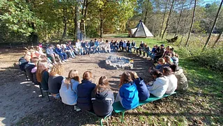 Gruppe sitzt im Kreis um eine Feuerstelle im Freien.