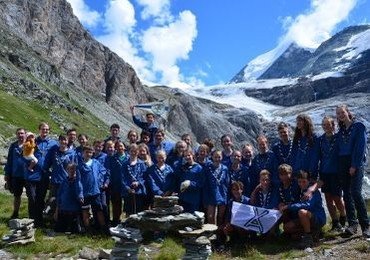 Gruppe von Personen in blauen Hemden posiert vor einem Gletscher.
